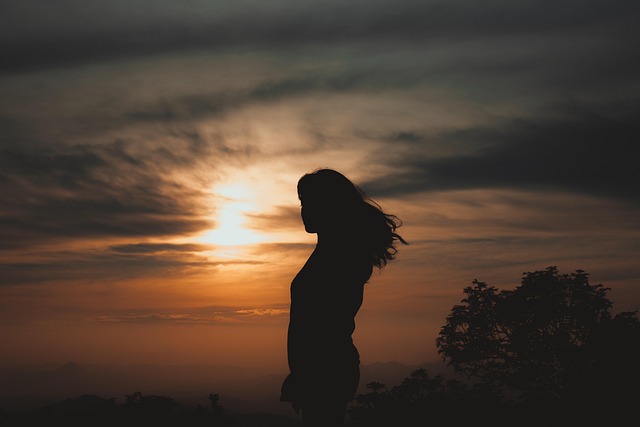 夕陽の光の中に静かに立つ女性のシルエット。夢が無意識を照らし、心を自由へ導く象徴的なイメージ。