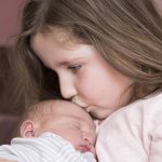 赤ちゃんを抱きしめて頬にキスする少女｜蟹座が象徴する家族愛と守る本能