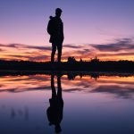 夕暮れの湖面に立つ人物のシルエットとその影｜Dream reflection and life stages