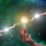 宇宙空間を背景に、光る電球に触れる手が象徴する直感と気づき。夢の意味や無意識とのつながりを示すイメージ写真