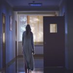 青い光に包まれた廊下を無意識に歩く人物の後ろ姿。 心と体が分離したような感覚、夢と現実の境界を象徴するイメージ。 A person walking unconsciously down a dimly lit hallway, symbolizing the boundary between consciousness and the unconscious in dreams.