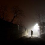 暗い夜道を一人で歩く人物。閉塞感や不安、光に向かう心を象徴しているイメージ