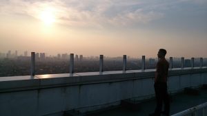 夕暮れの屋上から都市を見下ろし、未来を思索する人物の姿（水瓶座の象徴）