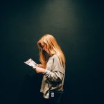 暗い背景の中で紙を見つめる人物。ビラに込められた意味や心のメッセージを静かに読み取る様子