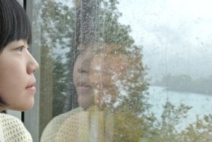 雨の窓越しに外を見つめる女性。静かに心が疲れているときのイメージ