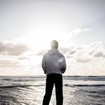 海を前に立つ人物。行方不明の夢が、人生の節目や心の移行を表していることを象徴。