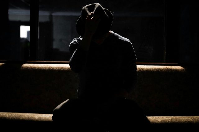帽子で顔を隠し、暗がりに座る人物のイメージ写真