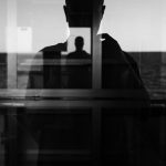 ガラス越しにシルエットが重なる人物のモノクロ写真