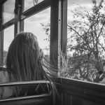 窓の外を見つめながら風に髪が揺れる人物の後ろ姿