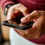 スマートフォンを手にしながら見つからない連絡先を思い出そうとするイメージ