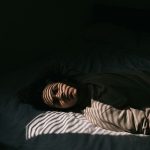 身体の不調と夢の関係のイメージとして使える、ベッドに横たわる人物の顔に影が落ちる様子