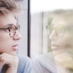 窓に映る自分を見つめながら考え込む人物のイメージ