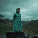 雨の森の中をレインコートを着て歩く人の後ろ姿。合羽やレインコートの夢のイメージ。