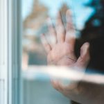 窓ガラス越しに手を当てる人物
