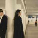 柱を挟んで背中合わせに立つ男女が、近いのに距離を感じる関係を表している