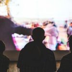 大きなスクリーンを見つめる人たちの後ろ姿