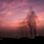 夕暮れの海辺に、ぼんやりと重なって見える人物の姿。変化の途中にある心や自己イメージの揺らぎを表すイメージ。